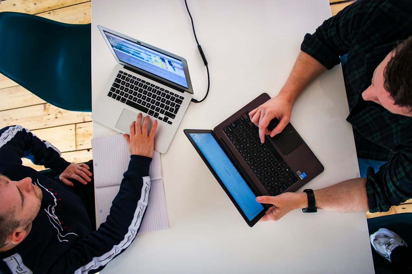 Twee mensen bekijken samen hun werk op laptops aan een tafel